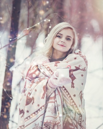 Pensive relax and happy girl with a warming drink sitting in the winter forest.の写真素材