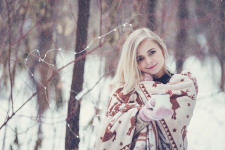 Pensive relax and happy girl with a warming drink sitting in the winter forest.の写真素材