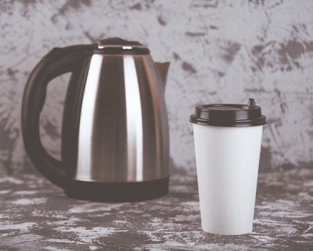 Working on the go. Coffee cup and electric kettle on grey stone table. Copy space.の写真素材