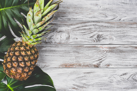 Green leaves monstera with one raw pineaple on white wooden background top view. Copyspace for your text, bannerの写真素材