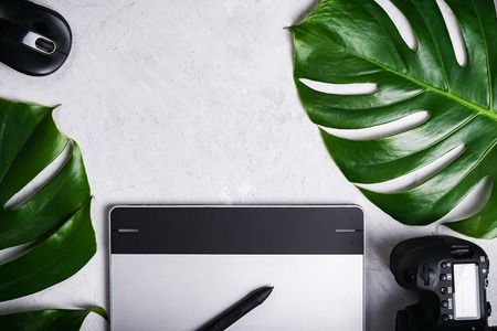 Close-up view of photographer's of graphic designer's workplace. Tablet, stylus, camera, optical wireless mouse, monstera green leaf.の写真素材