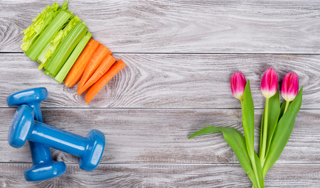 Spring flatlay sports composition with celery an carrots blue dumbbells and tulips on gray wooden background. Concept healthy lifestyle, sport and diet in spring. Top viewの写真素材