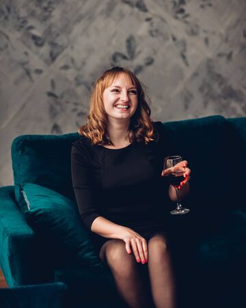 Attractive happy woman in little black dress and heels, with the red lips, fault holding a glass of wineの写真素材