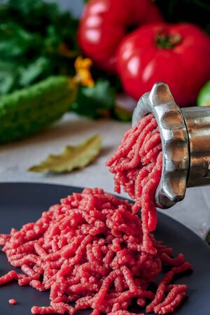Fresh red meat mincing with old metal manual grinder in close-up on grey stoneの写真素材