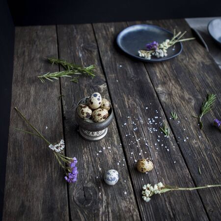 Quail  eggs in metal rustic bowl and black ceramic plates with white small flowers and splited salt...