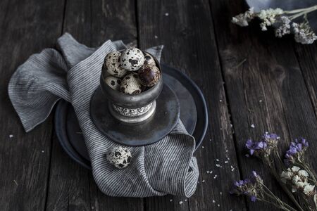 Quail  eggs in metal rustic bowl and black ceramic plates with white small flowers and splited salt...