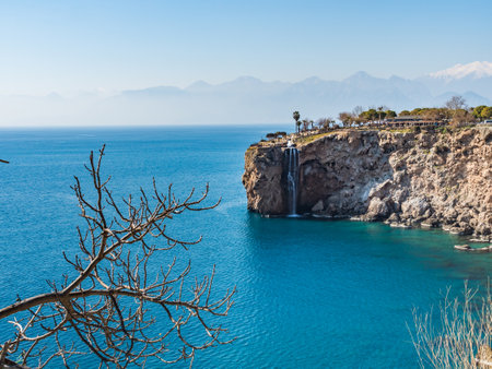 View of a waterfall that flows into the blue sea. Sunny day in Turkey on the seashore. Beautiful mountain landscape. Trees without leaves in the foreground. No people. copy space.の写真素材