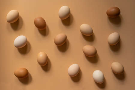 Eggs of different shades of brown lie randomly on a light brown background, top viewの写真素材