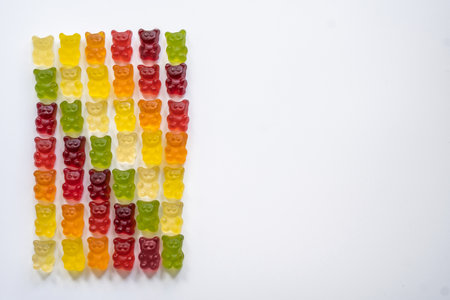 top view of multi-colored gummy bears arranged in rows by color as a gradient on a light background with negative space close-upの写真素材