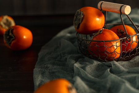 ripe persimmons in retro style metal basket on fabric runnerの写真素材
