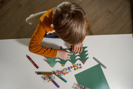 a boy decorates paper Christmas trees for Christmas