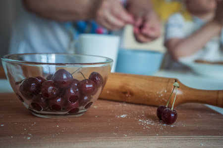 A bowl of cherry sits on a counter next to a rolling pin, close upの写真素材