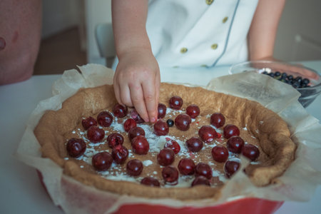 A child is putting cherries on a pie, close-upの写真素材