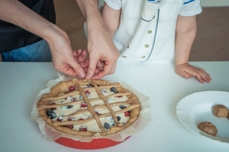A man and a child are cutting a pie with berries on top.の写真素材