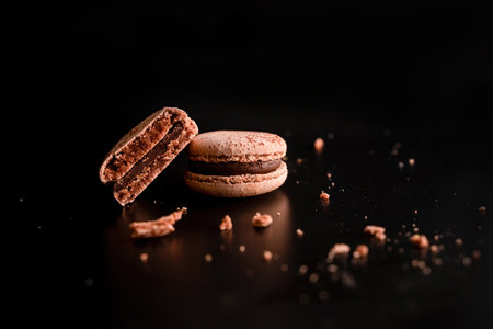 several chocolate macaroons cut in half on a dark background close up