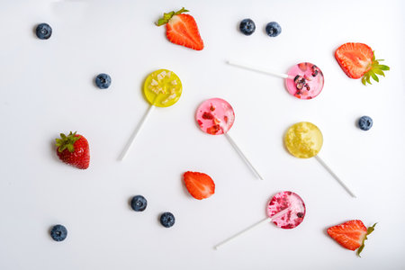 multi-colored homemade fruit lollipops lie on a white background next to various berries top viewの写真素材