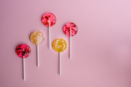red and yellow homemade fruit healthy lollipops lie behind the colors on a pink background with negative spaceの写真素材
