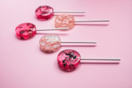 homemade fruit lollipops with pieces of fruit in different shades of pink on a pink backgroundの写真素材