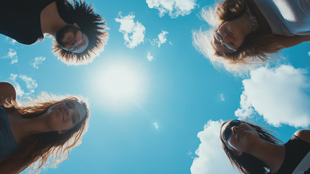 Four people are standing in a circle. The sun is shining brightly, and the sky is clear and blueの素材