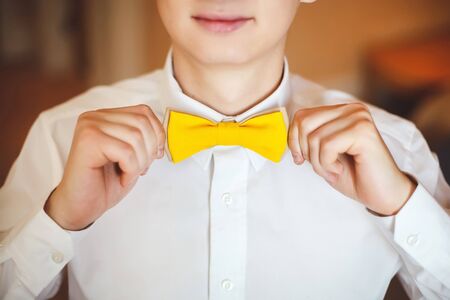 Portrait of happy smiling young man in a wedding costume and yellow butterfly tie. Closeup. Hands, lips.の写真素材