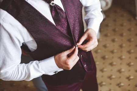 The groom buttons pink suit at the hotel.