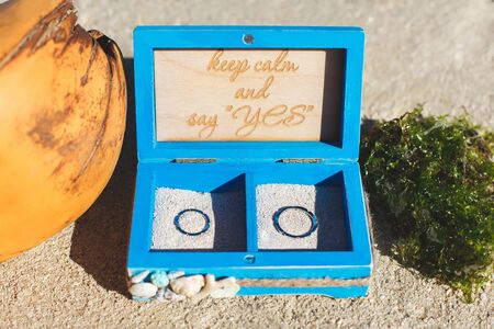 Wedding ring on the ocean in a wooden box. Sand. Beach. Coconut.