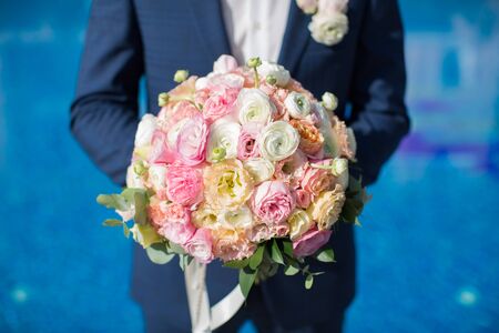 Beautiful bouquet of fresh flowers in the hands of the groom on the background of the pool at the hotel.の写真素材
