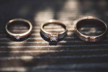 Three rings on wooden background. Engagement ring and two wedding bands on wooden table. White gold wedding jewelry.の写真素材