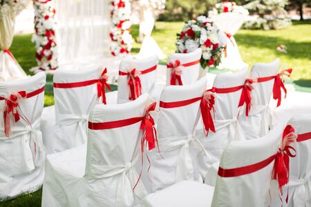 Wedding ceremony outdoors. White chairs with red ribbon.の写真素材