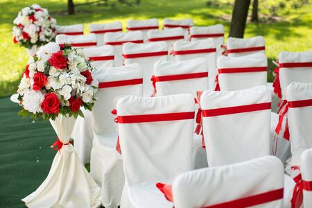 Wedding ceremony outdoors. White chairs with red ribbonの写真素材
