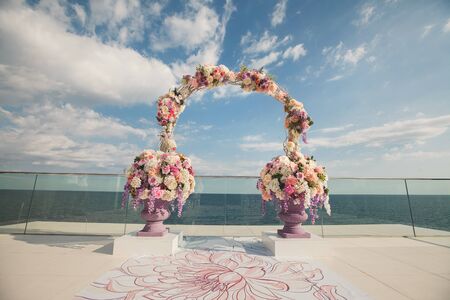 Wedding arch with fresh flowers on a sea background. Vases with fresh flowersの写真素材