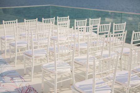 White chairs closeup on background of wedding arches peach color with flowers on the background of the seaの写真素材