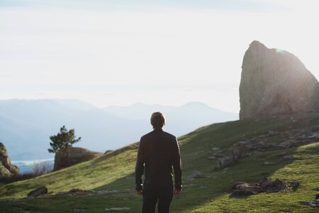 the silhouette of a man walking along the road to the mountain against the blue sky.