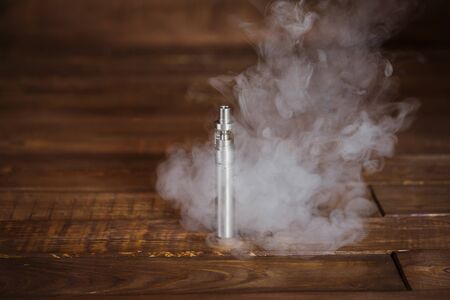 Electronic cigarette on a wooden table. Smoke.
