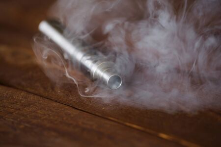 Electronic cigarette on a wooden table. Smoke.