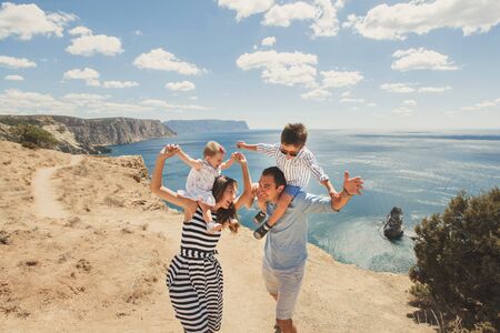 A happy family of four celebrating their lives against the backdrop of mountains and the sea.