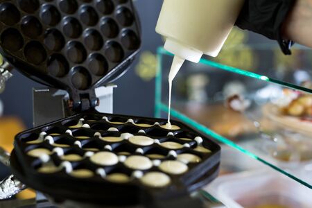 Pouring dough on waffle maker. Preparing Hong Kong waffle.の写真素材