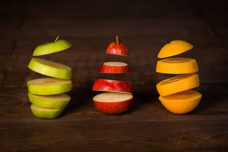 Apple, pear, orange cut in half frozen in the air on a black wooden background.