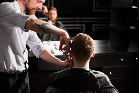 Master cuts hair and beard in the Barber shop. Hairdresser makes hairstyle using scissors and a metal comb.の写真素材