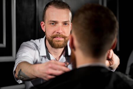 Master cuts hair and beard in the Barber shop. Hairdresser makes hairstyle using scissors and a...