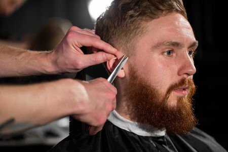 Master cuts hair and beard in the Barber shop. Hairdresser makes hairstyle using scissors and a...