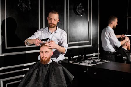 Master cuts hair and beard in the Barber shop. Hairdresser makes hairstyle using scissors and a...