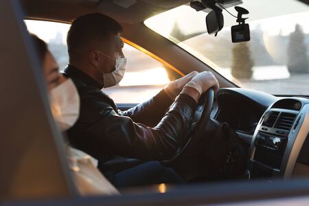 A man and a woman wearing medical masks and rubber gloves to protect themselves from bacteria and viruses while driving a car. masked men in the car. coronavirus, covid-19の写真素材