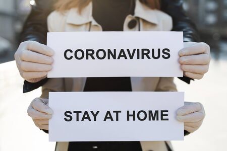 A woman and a man in protective medical masks hold a placard with the words stay at home and...