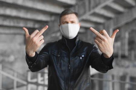 Go away from here. Young angry man with surgical medical mask showing fuck sign at camera. Coronavirus. covid 19.の写真素材