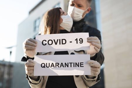 A woman and a man in protective medical masks hold a placard with the words Quarantine and Covid 19の写真素材