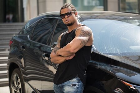 Black man in sunglasses standing near the car with modern building on background.の写真素材