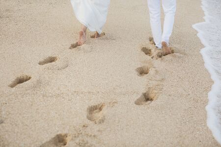 The bride and groom walk hand in the sand. footprints in the sand near the ocean.の写真素材