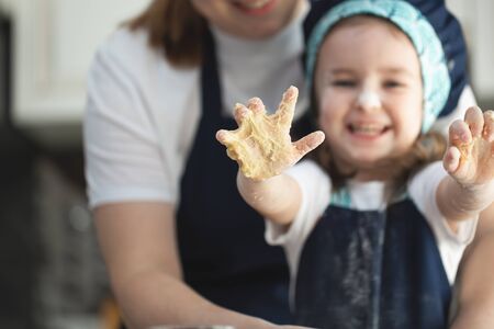 Mother and funny daughter showing hands in dough on kitchen.