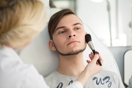 Professional Make-up artist doing young man makeup in studio.の写真素材